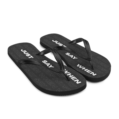 the capital flip-flops in black with bold white ‘just say when’ text and a subtle repeating pattern on the soles.